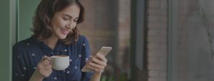 smiling girl looking at her cellphone while drinking coffee